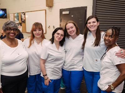 C.E.W.D. graduates in white scrubs posing together.