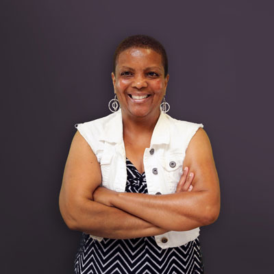 Denise Acres stands in front of a purple background.