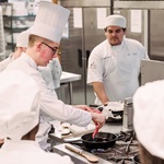 Students watch as a guest chef places meat into a skillet.