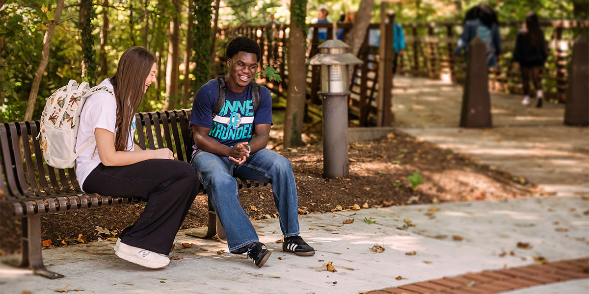 Two students sitting on a bench talking.