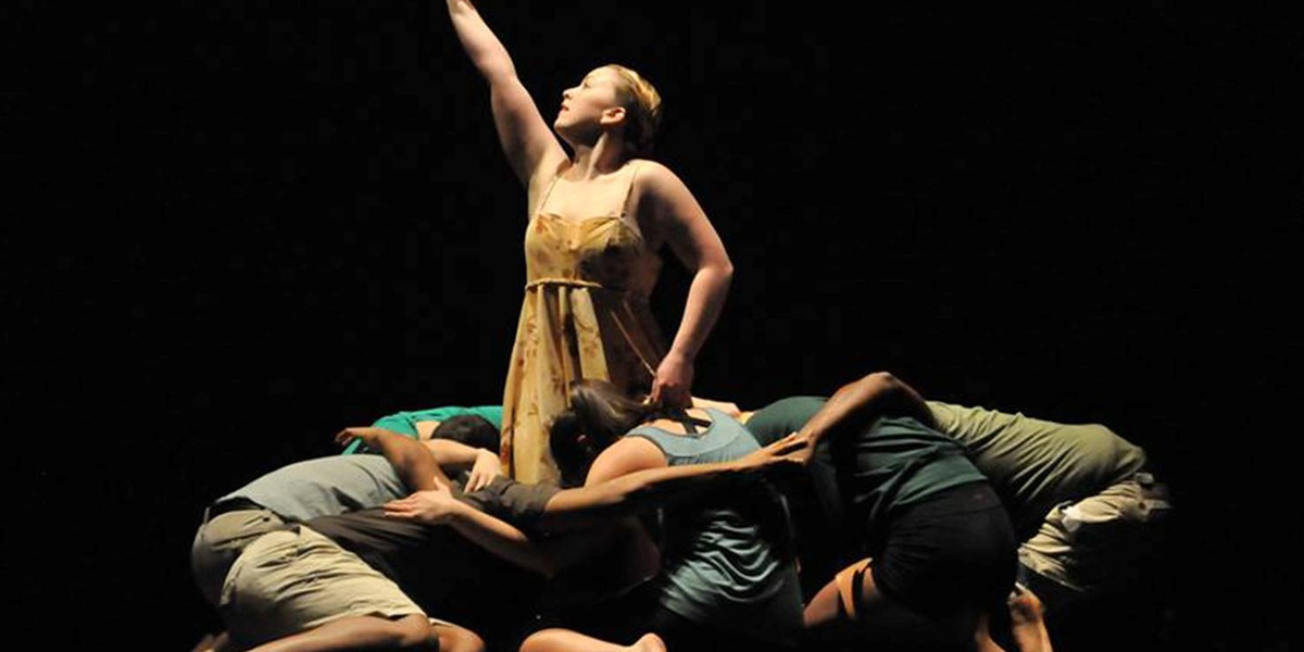 AACC dancers huddle around a single dancer on stage.