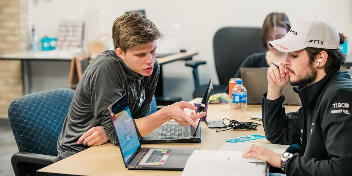 Students working with one another at a table with laptops.