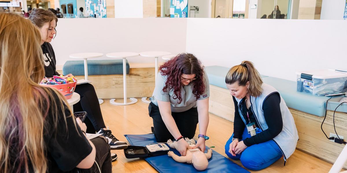 Instructor showing a person how to perform CPR on a baby mannequin