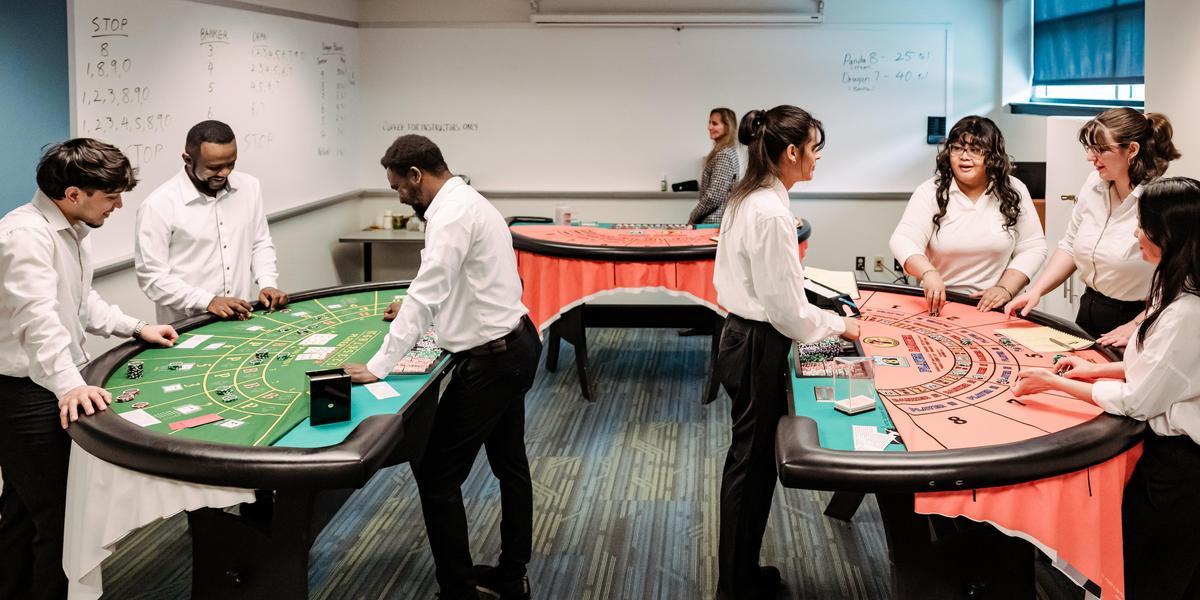 Students stand at gaming tables as an instructor looks on.