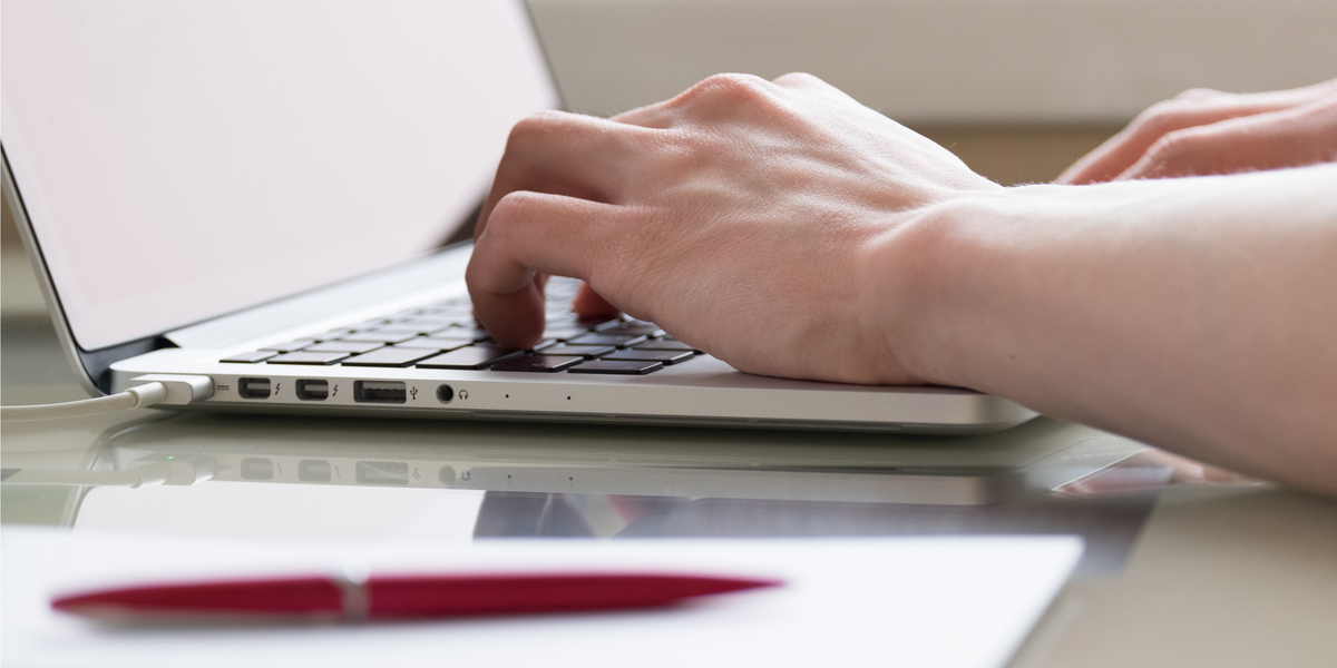 person typing on a computer with pad and pen in foreground