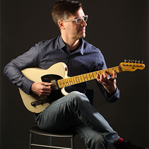 Ian Wardenski sitting on a chair and holding a guitar
