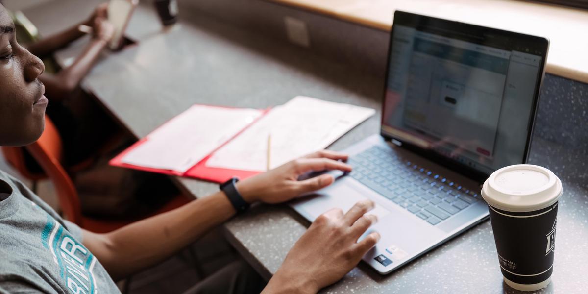 A student types on a laptop with an open notebook sitting next to them.
